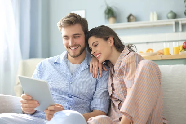 Pareja joven viendo contenido multimedia en línea en una tableta sentada en un sofá en la sala de estar. —  Fotos de Stock