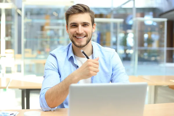 Porträtt av en ung man som sitter vid sitt skrivbord på kontoret. — Stockfoto