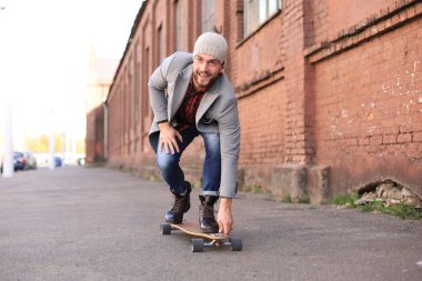 Şehirde sokakta uzun tahta üzerinde gri ceket ve şapka yakışıklı genç adam. Kentsel kaykay konsepti.