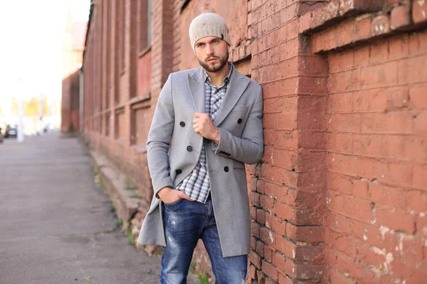 Stadtleben. Stilvoller junger Mann in grauem Mantel und Hut steht auf der Straße in der Stadt. — Stockfoto