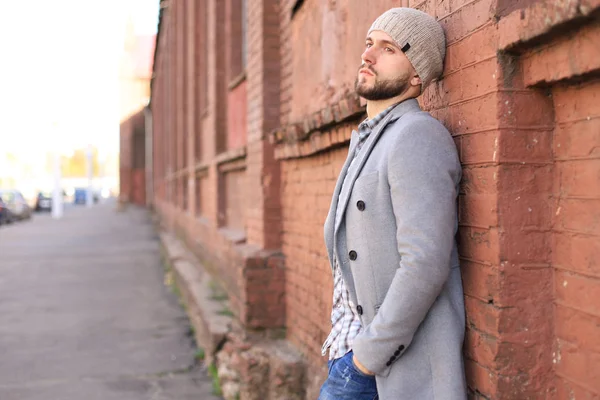 Vida en la ciudad. Joven con estilo en abrigo gris y sombrero de pie en la calle de la ciudad . — Foto de Stock