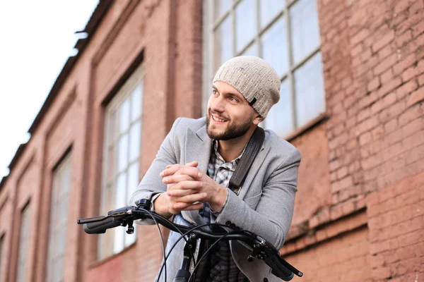 灰色のコートと帽子を着たハンサムな若者が自転車で立っている. — ストック写真