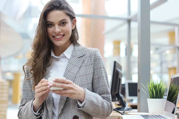 Belle femme d'affaires souriante debout dans le bureau avec une tasse de café . — Photo