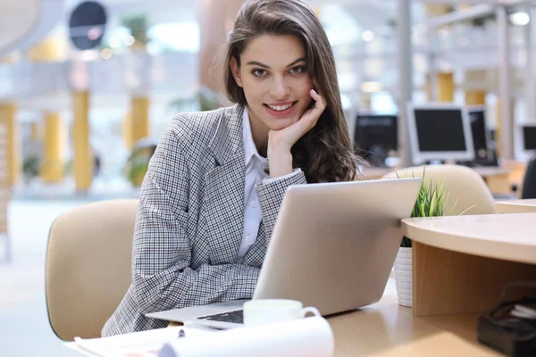 Πορτρέτο μιας χαρούμενης νεαρής επιχειρηματία που κάθεται στο τραπέζι στο γραφείο και κοιτάζει την κάμερα. — Φωτογραφία Αρχείου