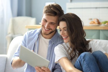 Genç bir çift, oturma odasındaki kanepede oturup internetten medya içeriğini izliyor..