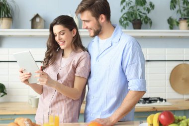 Pijama mutlu genç çift bir tablet online içerik izlerken ve evde mutfakta yemek yaparken gülümseyerek.