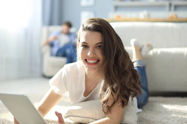 Sonriendo hermosa mujer usando el ordenador portátil con el hombre borroso en el fondo en casa . —  Fotos de Stock