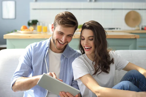 Pareja joven viendo contenido multimedia en línea en una tableta sentada en un sofá en la sala de estar. —  Fotos de Stock