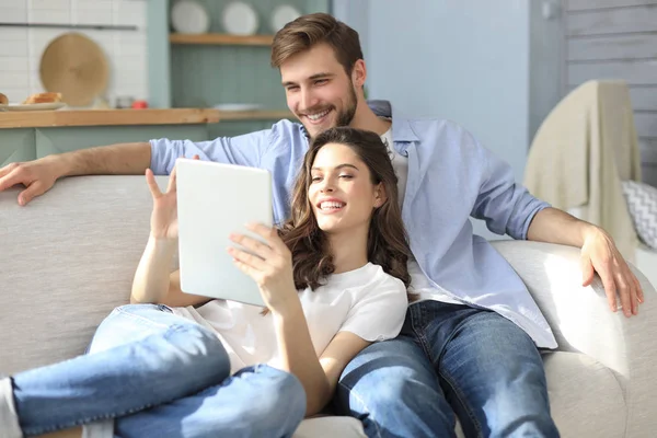 Pareja joven viendo contenido multimedia en línea en una tableta sentada en un sofá en la sala de estar. —  Fotos de Stock