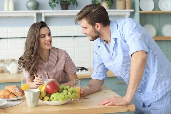 Beautiful young couple in pajamas is looking at each other and smiling while cooking in kitchen at home. — Stock Photo, Image