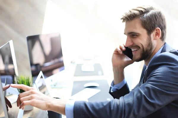 Hombre de negocios moderno analizando datos usando la computadora y hablando por teléfono mientras está sentado en la oficina . —  Fotos de Stock