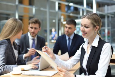 Çalışanlarıyla birlikte çalışan bir iş kadını, modern aydınlık ofiste arka planda çalışan insanlar..