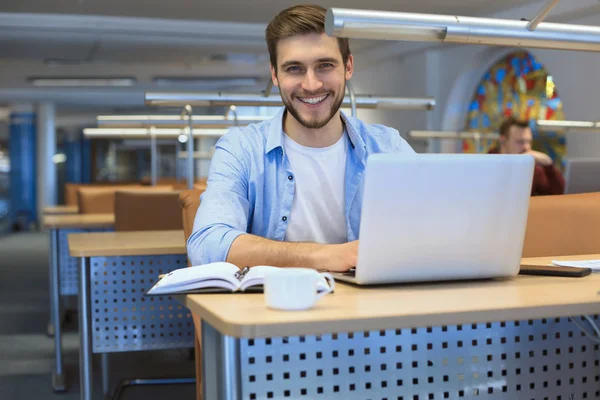 Joven estudiante trabajando en portátil en la biblioteca . — Foto de Stock