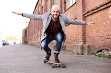 Şehirde sokakta uzun tahta üzerinde gri ceket ve şapka yakışıklı genç adam. Kentsel kaykay konsepti.