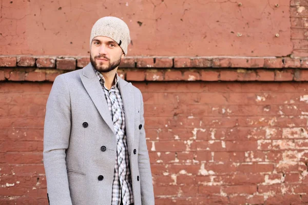 City life. Stylish young man in grey coat and hat standing on the street in the city.