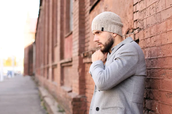 Vida en la ciudad. Joven con estilo en abrigo gris y sombrero de pie en la calle de la ciudad . — Foto de Stock