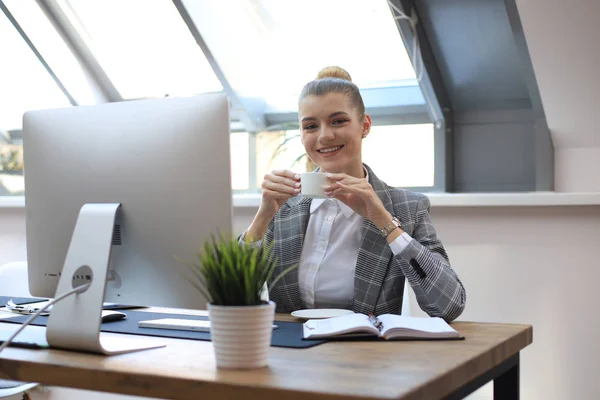 Atractiva mujer de negocios sonriente sentada en la oficina con una taza de café . — Foto de Stock