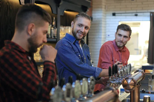 Guapo camarero está sonriendo y llenando un vaso de cerveza mientras está de pie en el mostrador del bar en el pub . —  Fotos de Stock