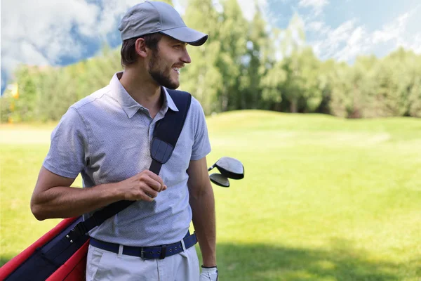 Portrait of male golfer carrying golf bag while walking by green grass of golf club. — Stock Photo, Image
