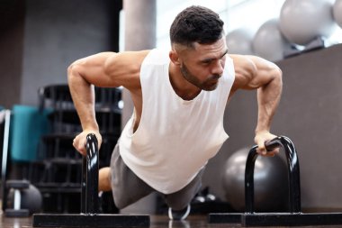 Spor salonunda barlar ile yatay şınav yapıyor fit ve kaslı adam.