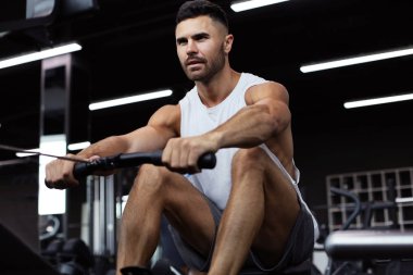 Spor salonunda kürek makinesi kullanan fit ve kaslı adam.