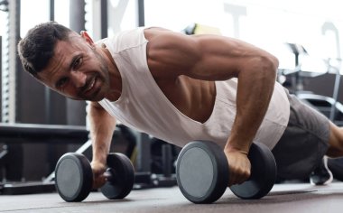 Spor salonunda dambıllarla yatay şınav yapan fit ve kaslı adam.