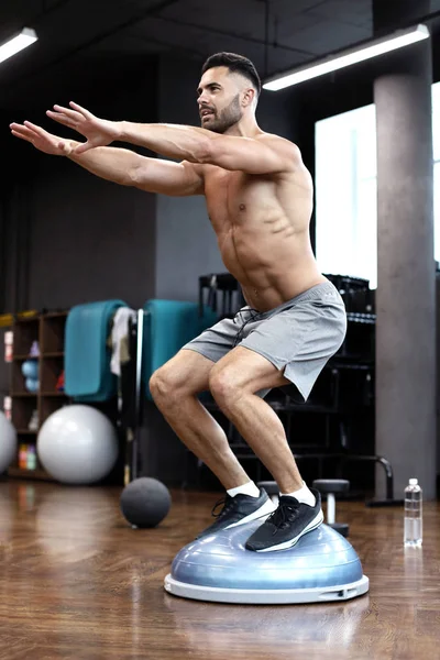 Ajuste atleta realizar ejercicio en el hemisferio gimnástico Bosu ball en el gimnasio . — Foto de Stock