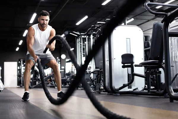 Athletic young man with battle rope doing exercise in functional training fitness gym. — Stock Photo, Image