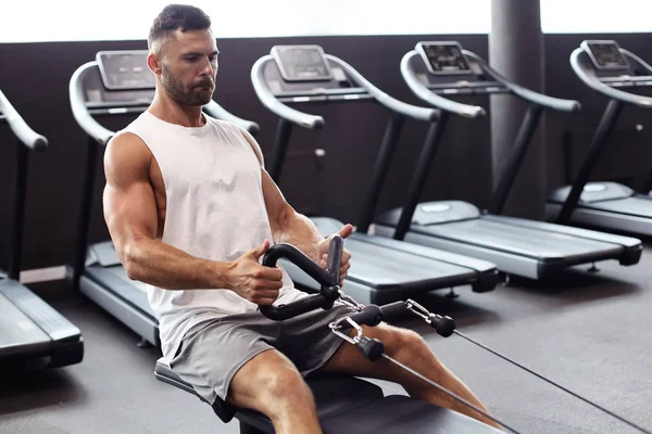 Dopasowanie i muskularny Człowiek wykonujący ćwiczenia na symulatorze. — Zdjęcie stockowe