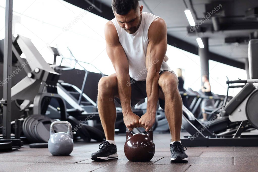 Fit and muscular man focused on lifting a dumbbell during an exercise class in a gym.