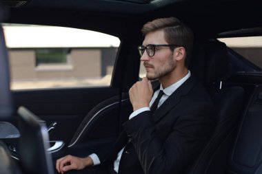 Lüks arabada otururken gözlük elini tutmak düşünceli kendinden emin işadamı.