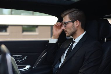 Lüks arabada otururken gözlük elini tutmak düşünceli kendinden emin işadamı.