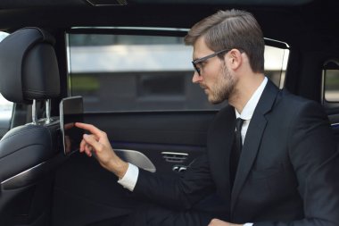 Düşünceli genç işadamı lüks arabada oturan ve tabletini kullanarak.