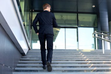 Şık başarılı işadamı ofis binasının merdivenlerinden çıkıyor.