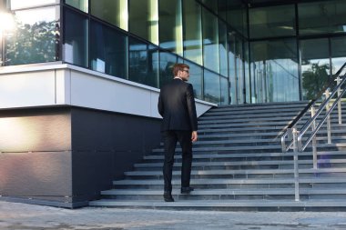 Şık başarılı işadamı ofis binasının merdivenlerinden çıkıyor.