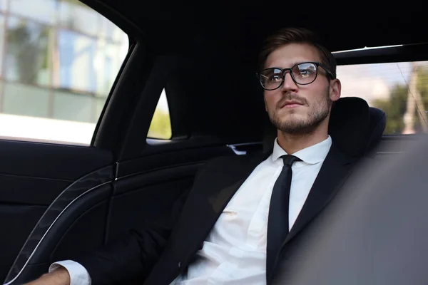 Pensiero uomo d'affari fiducioso in completo con occhiali guardando altrove mentre seduto in macchina . — Foto Stock