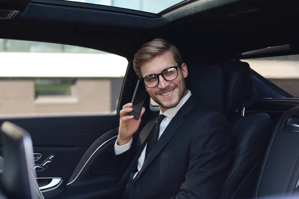 Hombre de negocios guapo hablando con teléfono sentado con el ordenador portátil en el asiento trasero del coche . —  Fotos de Stock