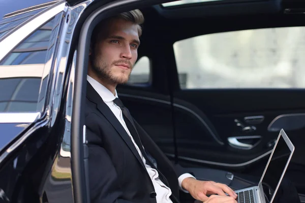 Продуманий впевнений бізнесмен сидить у розкішному автомобілі і використовує свій ноутбук . — стокове фото