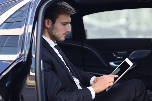 Doordachte jonge zakenman zittend in de luxe auto en het gebruik van zijn Tablet. — Stockfoto