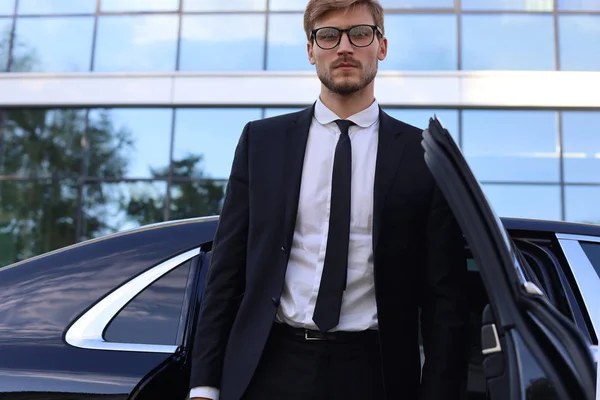 Beau jeune homme d'affaires sérieux debout près de sa nouvelle voiture confortable et aller au bureau . — Photo