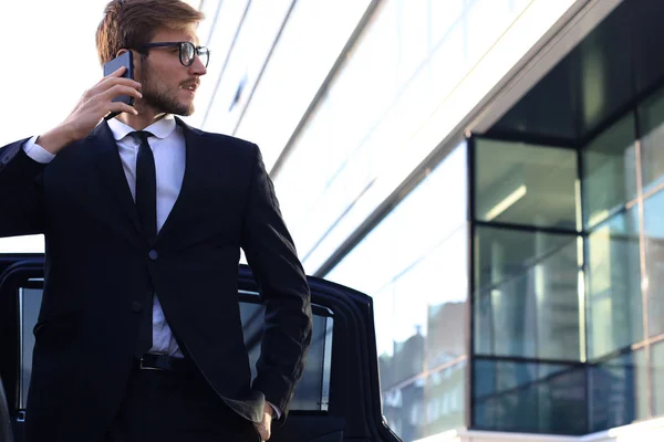 Knappe serieuze jonge zakenman staande in de buurt van zijn comfortabele nieuwe auto en naar het kantoor gaan. — Stockfoto