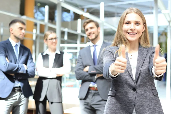 Concepto de negocio atractiva mujer de negocios con el equipo en la oficina mostrando pulgares hacia arriba . — Foto de Stock