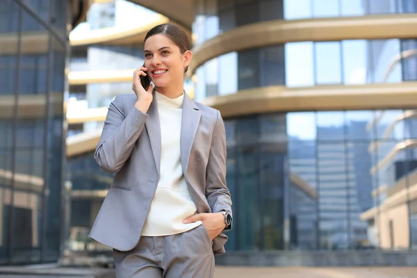 Portrait de femme d'affaires souriante élégante en vêtements à la mode appelant sur téléphone mobile près du bureau. — Photo