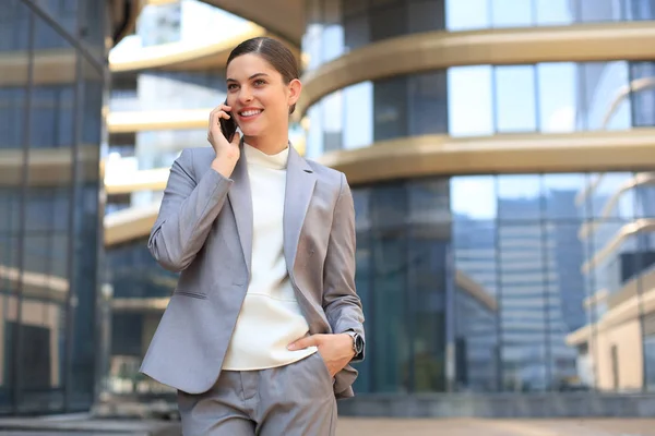 Arckép elegáns mosolygós üzletasszony divatos ruhák hívás mobiltelefon közelében iroda. — Stock Fotó