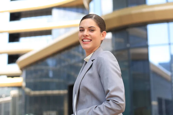 Attrayant jeune femme en costume regardant la caméra et souriant tout en se tenant à l'extérieur. — Photo