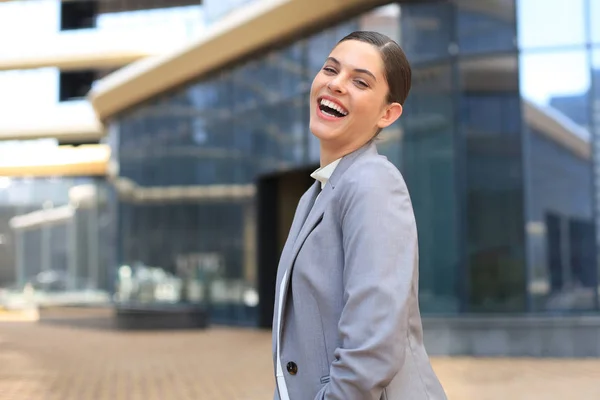 Attrayant jeune femme en costume regardant la caméra et souriant tout en se tenant à l'extérieur. — Photo