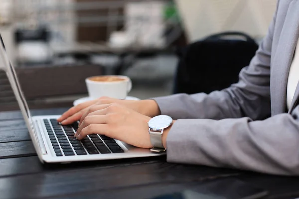 Negócios mulher mãos em terno está digitando em um laptop no café de rua. — Fotografia de Stock