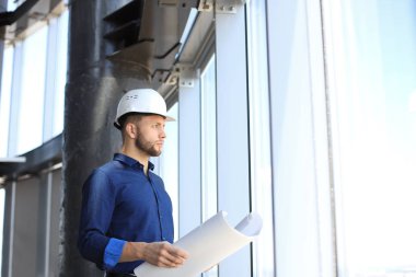 Ofiste bir pencereye karşı dururken planı inceleyen gömlek li kendinden emin genç adam.