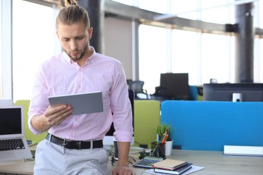 Ofiste otururken dijital tablet kullanarak çalışan genç modern işadamı.