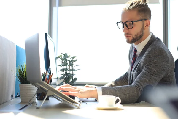 Jó kinézetű fiatal férfi teljes öltönyt használ laptop ülve az irodában. — Stock Fotó
